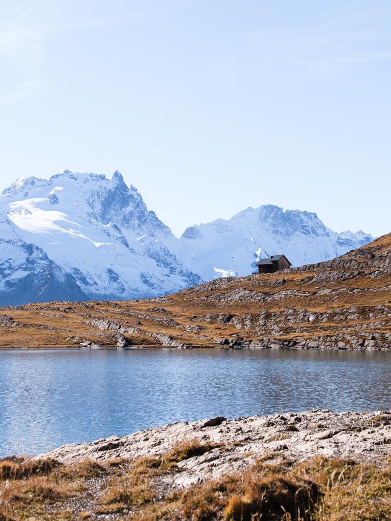 Paysage automnal alpin avec lac turquoise et sommets enneigés.