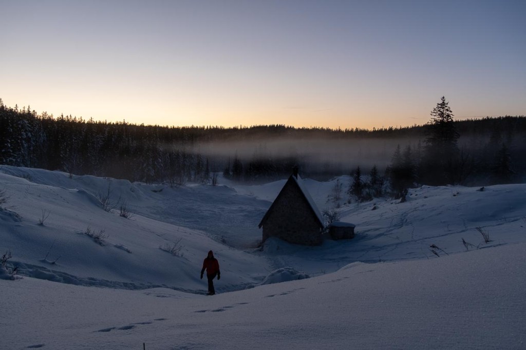 Coucher de soleil sur les Hauts Plateaux du Vercors, silhouette d’une cabane solitaire dans la neige avec randonneur